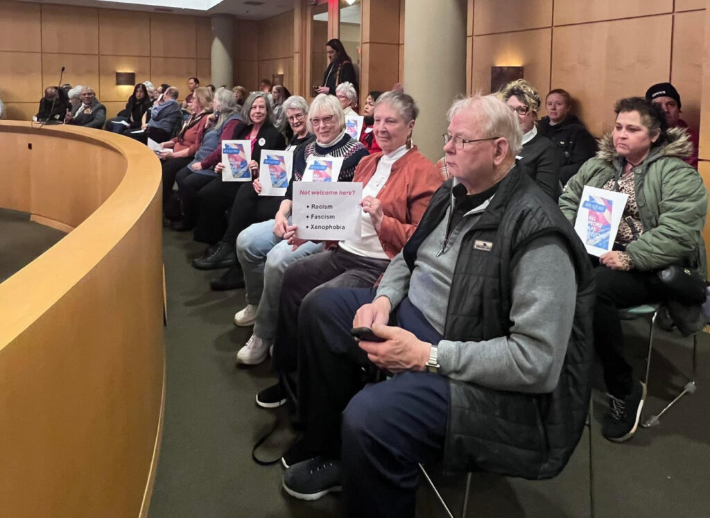 Several LWVGR members, plus other sympathizers, hold up photos of the welcome sign at the Rockford City Council meeting Feb. 24, 2025.